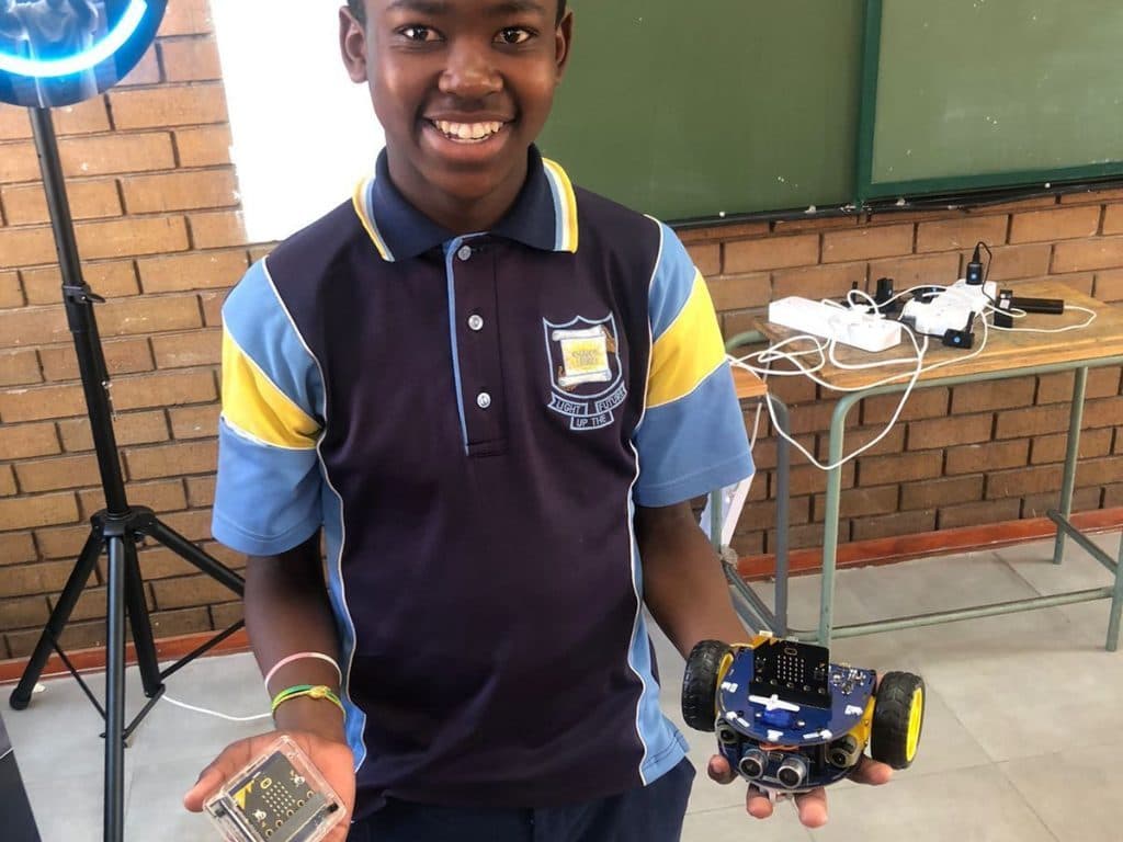 Learner proudly holding a micro:bit robot car built during a coding lesson