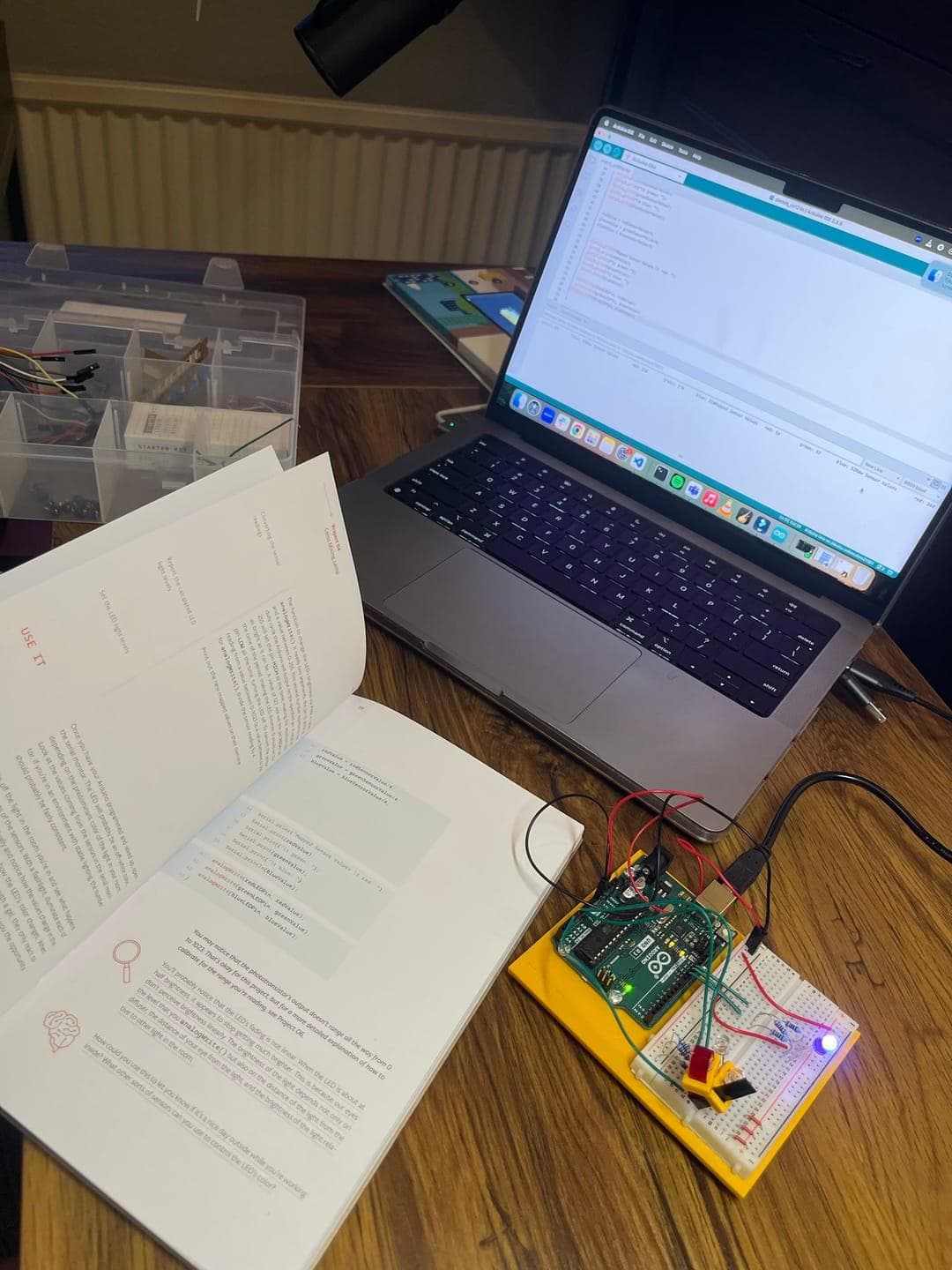 Arduino board and laptop on desk with open guidebook