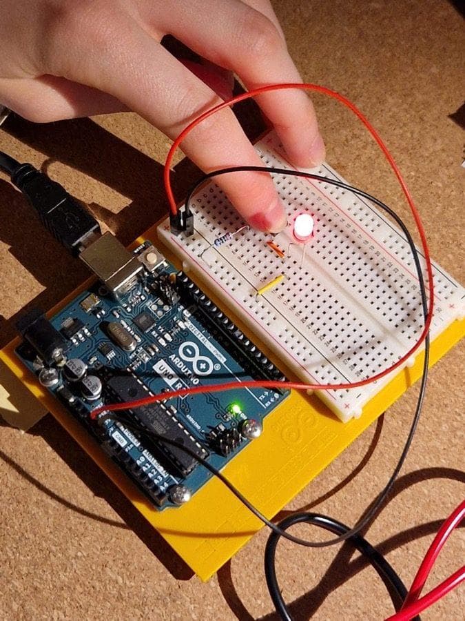 Finger pressing a button with LED lit up on an Arduino breadboard