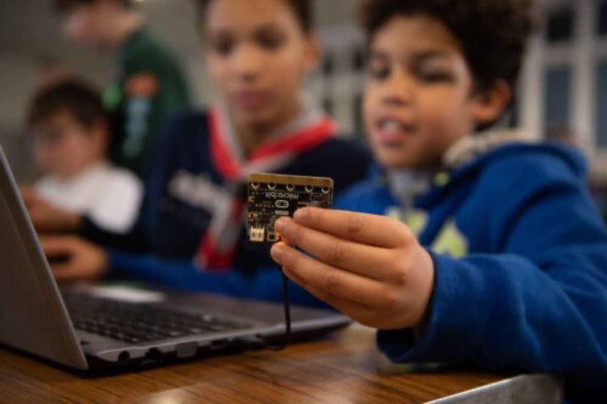 Child holding up a micro:bit board to the camera, enthusiastically showing their project