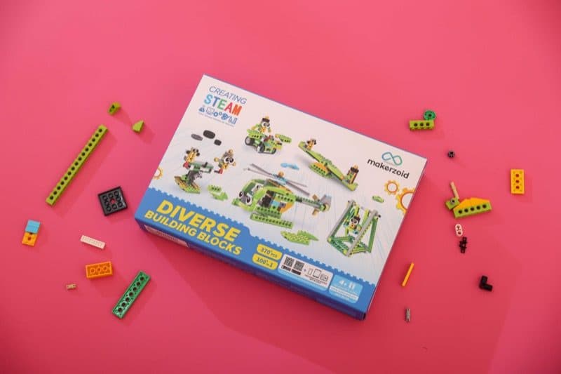 Makerzoid box on a pink background with building pieces arranged around it