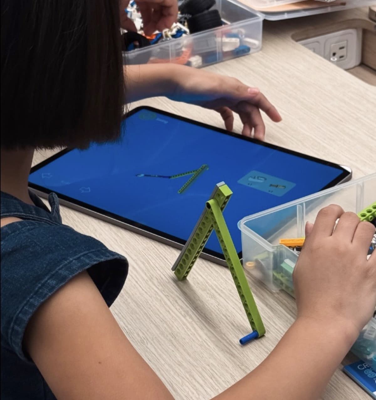 Girl at a desk following 3D building instructions on a tablet screen with Makerzoid blocks in front of her