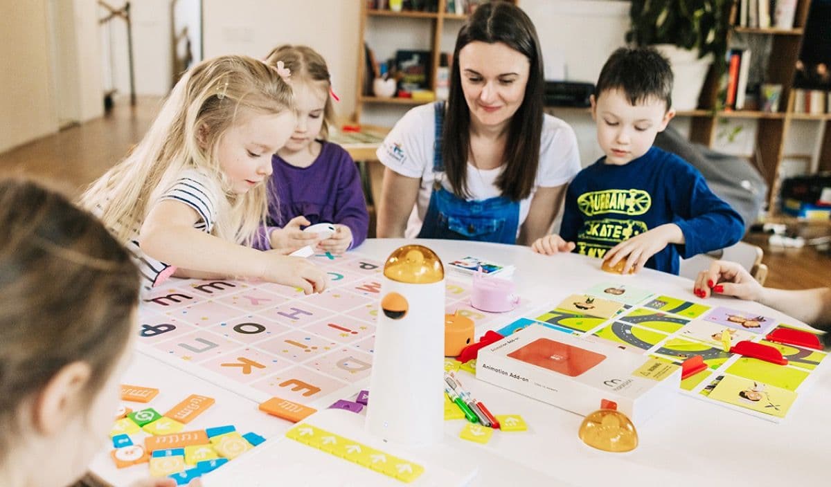 Young learners sitting at a table working together on MatataStudio coding challenges with their teacher
