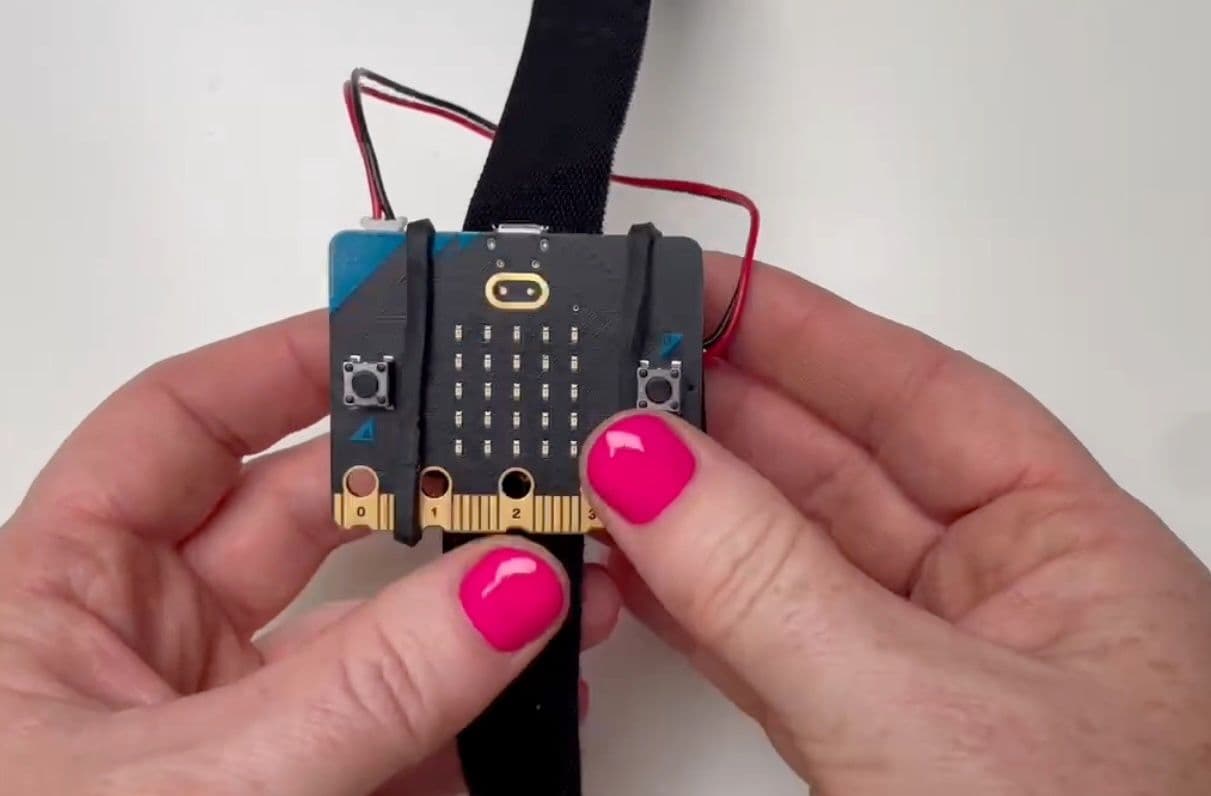 Hands holding a BBC micro:bit with the wearable strap attached