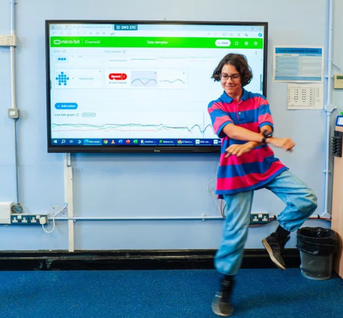 Child dancing in front of a projector screen with a micro:bit wearable on their wrist