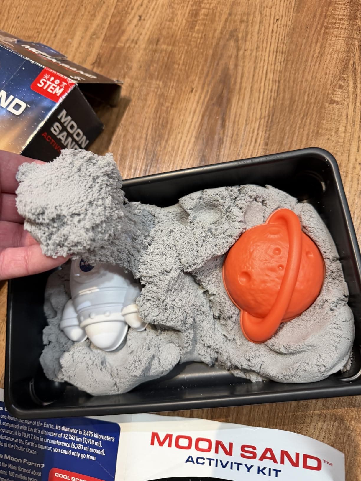 Hand holding a ball of moon sand above the play tray