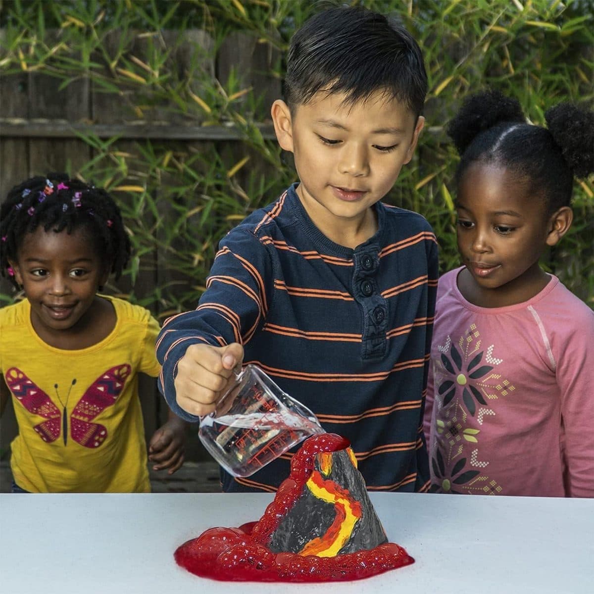 Three children watching their volcano erupt with fizzing lava