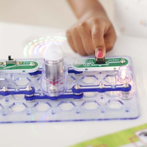 Finger pressing a switch on Snap Circuits board with the colour-changing fan spinning