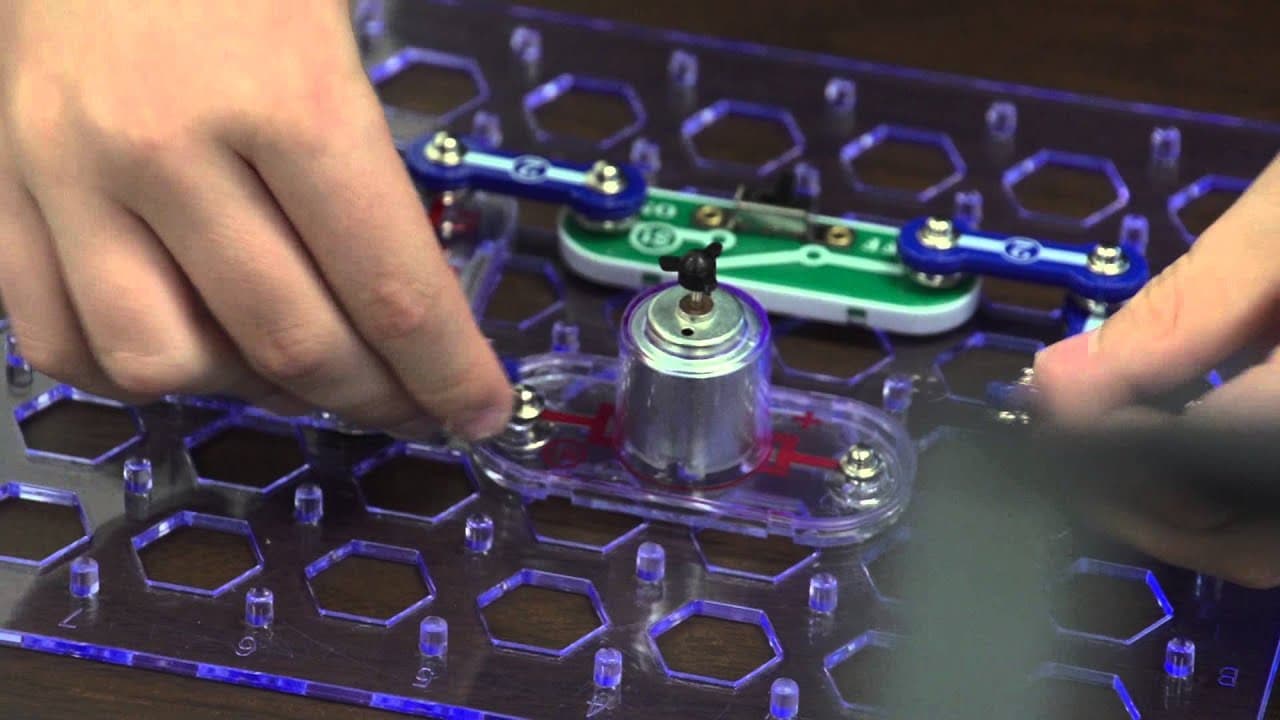 Fingers snapping circuit pieces onto the Snap Circuits base grid